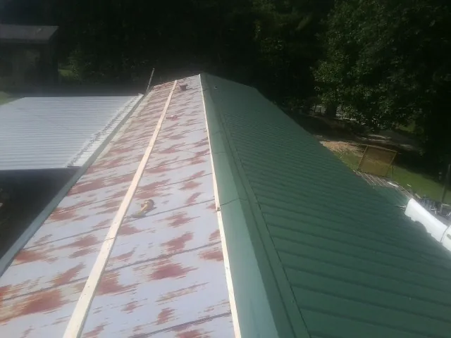 Old rusted panels beside newly installed green metal roofing — Wind Damage Roof Repair by Roofing Brothers in Owensboro