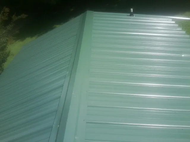 New green metal panels meeting at the ridge of a roof — Flat Roof Repair work by our crew in Owensboro