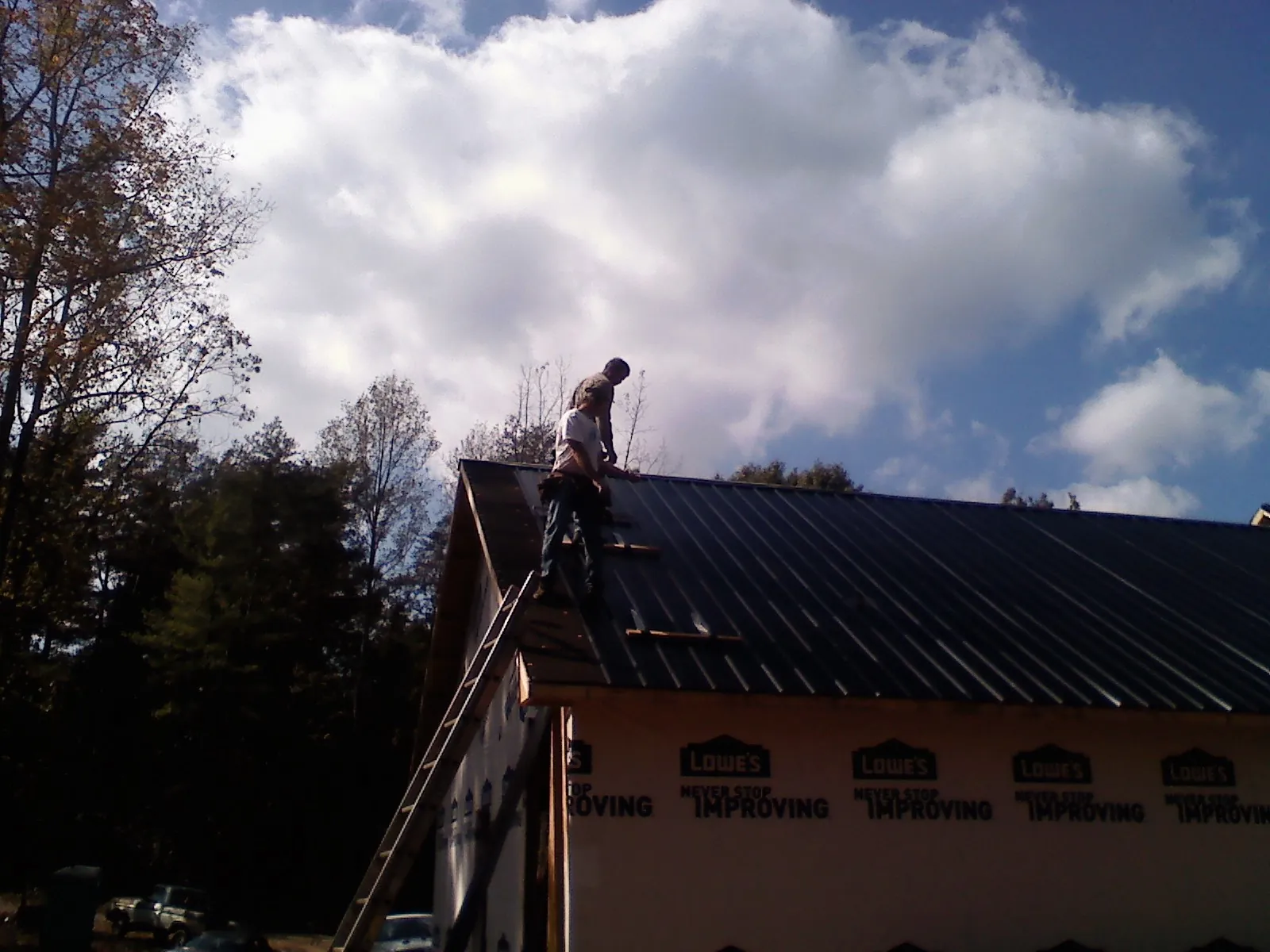 Roofer fastening dark metal panels high against a cloudy sky, from a Roof Inspection job in Owensboro