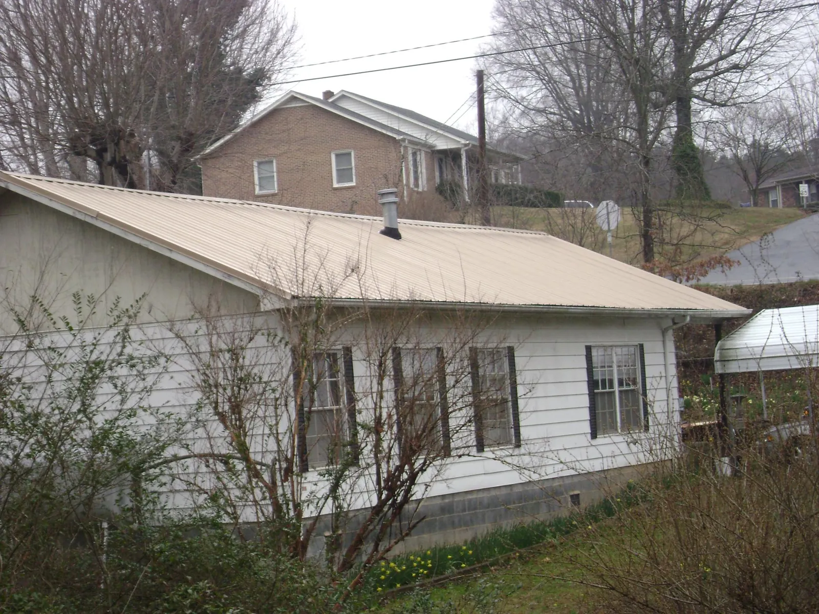 Tan metal roof on a white sided house set into a hillside — Commercial Roofing by Roofing Brothers in Owensboro